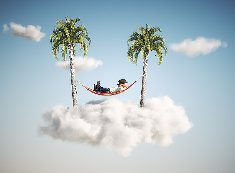 在云中两棵棕榈树之间的吊床上睡觉的人。