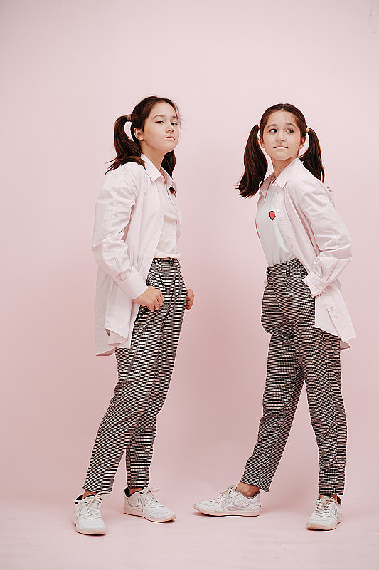 时尚的双胞胎女孩分层白衬衫在粉红色的背景。