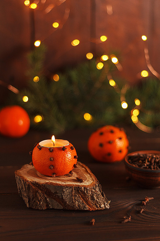 用冷杉树枝和圣诞彩灯装饰的桌子上的木架上放着一个橘红色的烛台。手工制作的。副本的空间。垂直图
