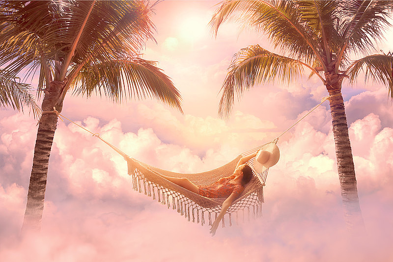 梦幻的夏天屏保与放松的年轻女子在色彩柔和的云彩之间的吊床上放松。