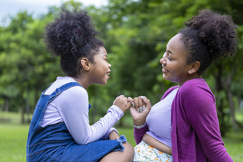 图为，在公园举行夏日野餐的非裔美国母亲，为了爱和幸福的概念，正在向年幼的女儿许下小指承诺