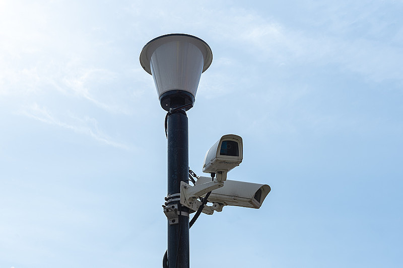 在蓝天的衬托下，监控摄像头安装在灯柱上。监控摄像头。城市的安全。