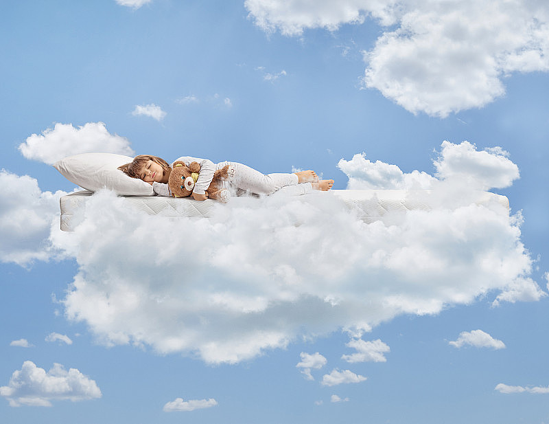 小女孩穿着睡衣，抱着泰迪熊，睡在云朵上