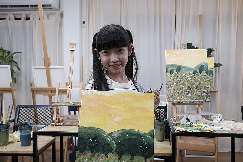 亚洲女孩展示她的画，自豪地与丙烯彩绘在画布上。