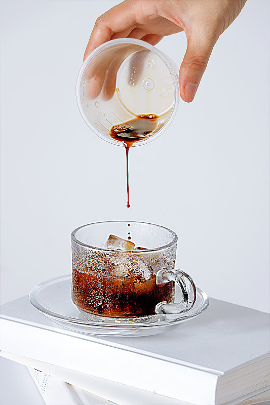 垂直镜头:一只手逐渐往白色背景上有冰块的杯子里加入咖啡