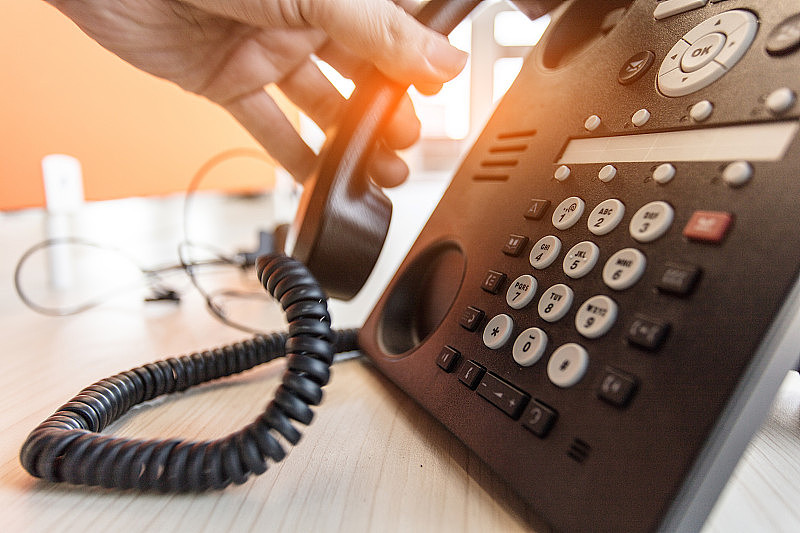 员工用手触摸桌子上的电话听筒来联系客户或接听电话，热线概念