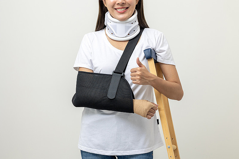 年轻的亚洲妇女断了胳膊和腿被隔离。妇女戴上石膏夹板，拄着拐杖。病人佩戴带颈圈的吊带支撑臂。人身保险及意外事故