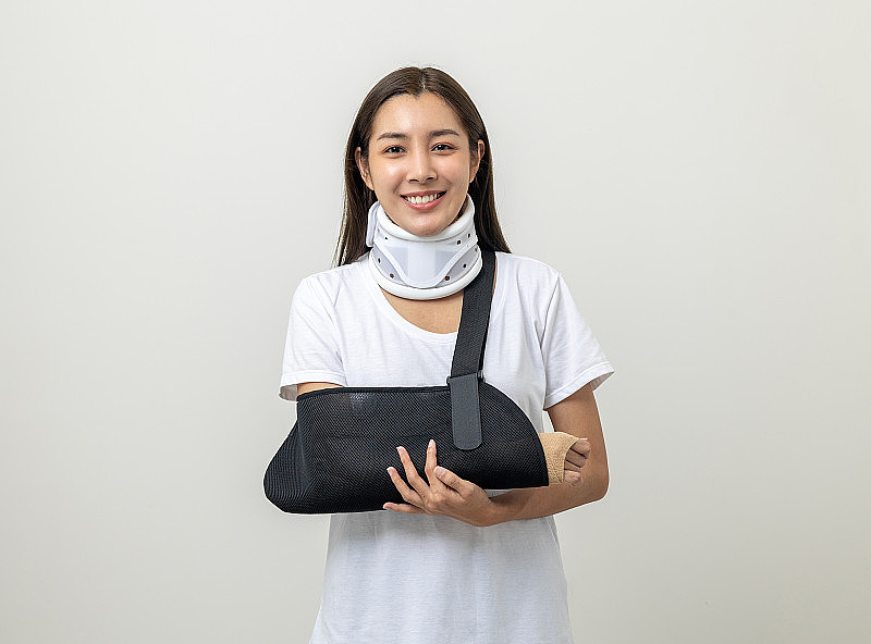 快乐的年轻亚洲女子在孤立的背景下断了胳膊。亚洲女性把石膏绷带石膏夹板。意外受伤后佩戴吊带支撑臂的病人。人身保险及意外事故