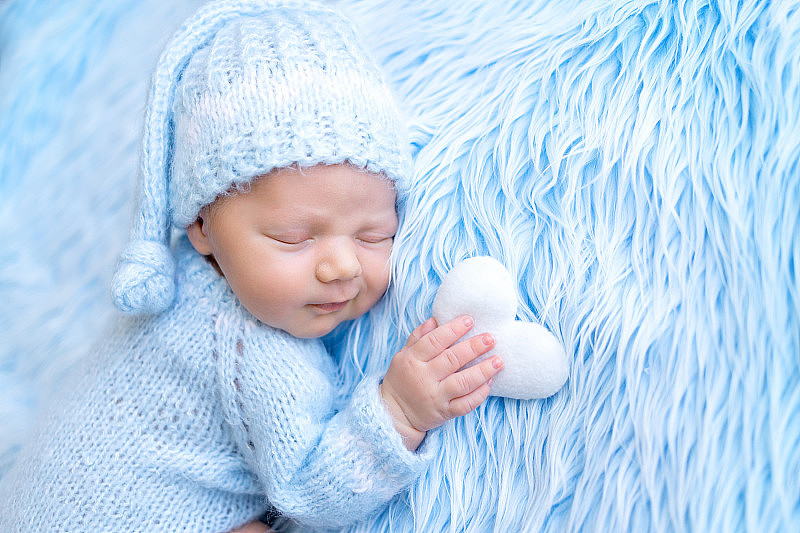 刚出生的宝宝手里拿着心形玩具，在蓝色背景上甜蜜地睡觉，健康的宝宝睡觉