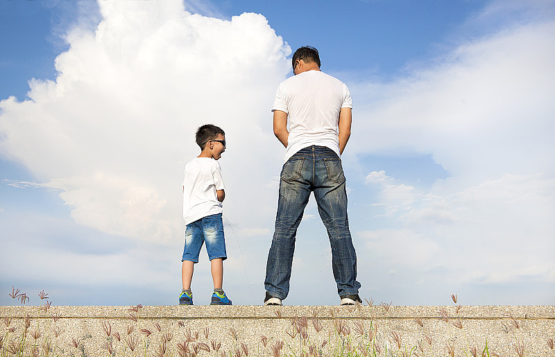 父亲和儿子站在一个石头平台上一起小便