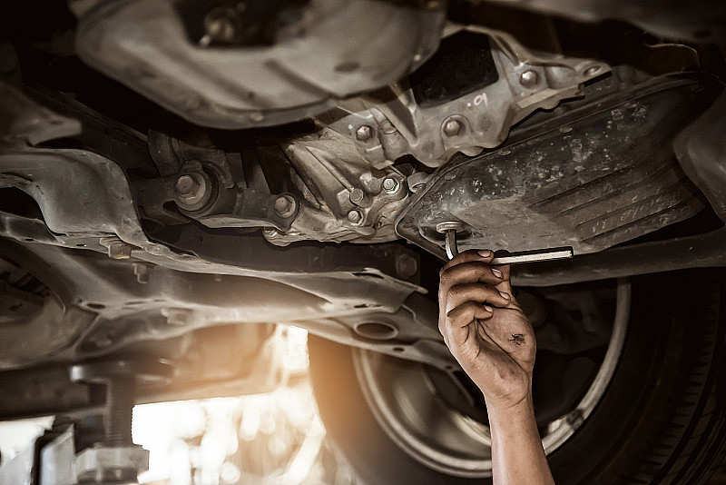 一辆汽车正在修车厂检查是否更换机油，修理工的手在下面的特写。