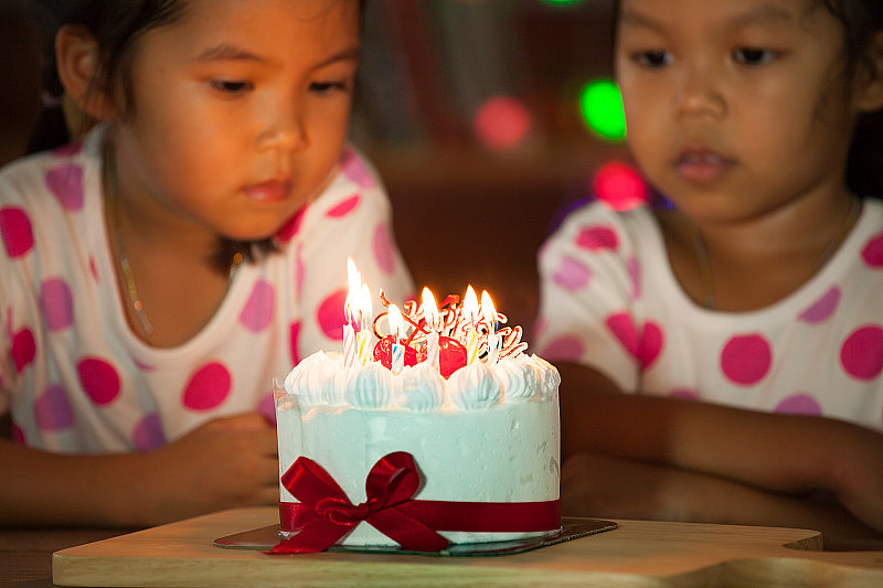 快乐的双胞胎两个亚洲小女孩庆祝生日和吹蜡烛的蛋糕