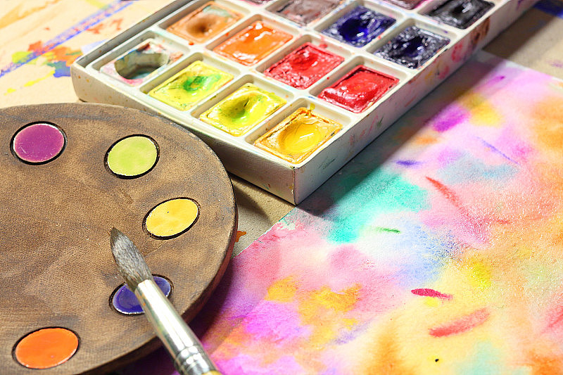 陶瓷板作为艺术调色板，用画笔和彩色水彩颜料在彩色抽象画的背景上作画。