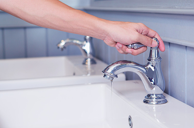 手工打开公共厕所的银色水龙头或带有白色洗涤槽的水龙头。