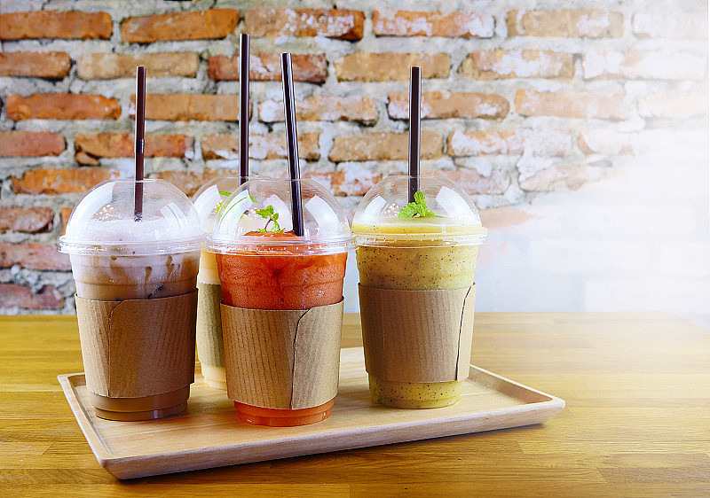 冰沙和冰咖啡在塑料杯上的木托盘和砖墙背景咖啡馆。不谈饮料的概念。