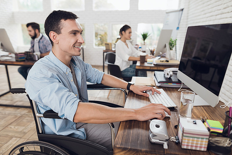 坐轮椅的残疾人在办公室用电脑工作。