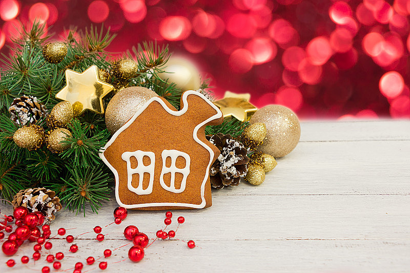 金色的圣诞装饰，姜饼形状的房子，白木背景上的树枝，红色的米糠。贺卡，文字空间