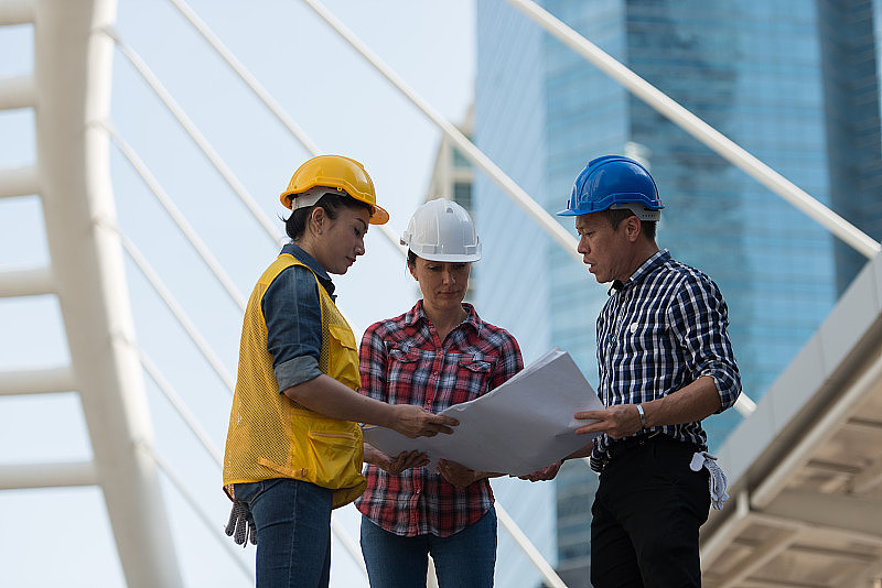 亚洲工程师小组持蓝图图纸进行现场施工咨询。在城市背景。团队合作理念