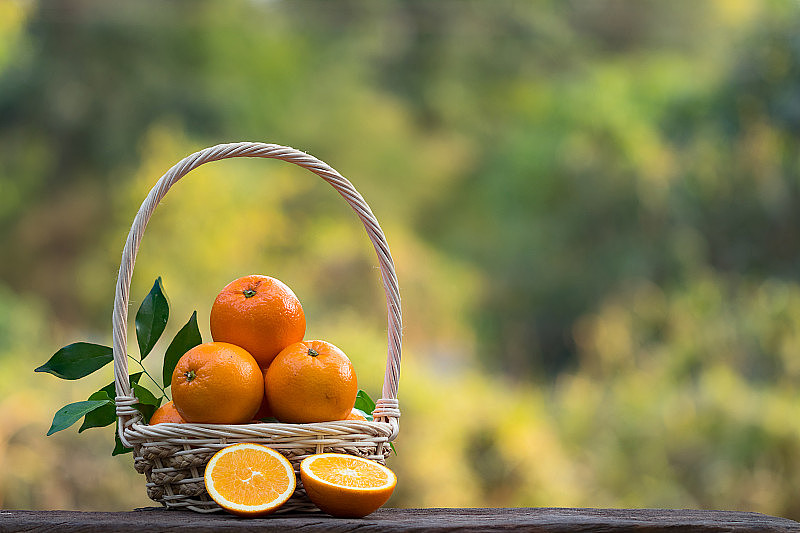 篮子里的橘子和把橘子切成两半的木桌放在绿色的米糠背景上