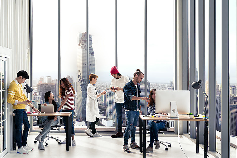成功的多民族商务团队在日常工作中创造性的生活方式，站在一起，坐着，交谈在现代的办公室，以广泛的视角。年轻忙碌多样化的团队合作或员工理念。
