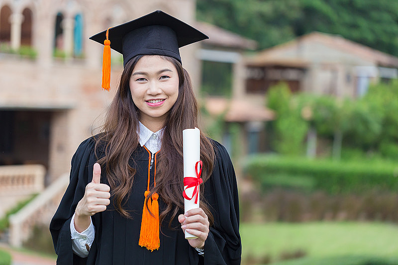 美丽迷人的亚洲女学生毕业生戴着帽子和礼服，手拿证书庆祝，在毕业典礼上感到自豪和幸福，教育成功的概念