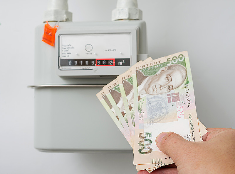 手里拿着乌克兰格里夫纳的账单，放在家里的天然气表前。象征性的图像为冬天的供暖，概念。选择聚焦,特写。
