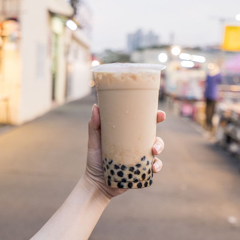 一名年轻女子正拿着塑料杯的红糖奶茶在台湾夜市,台湾美食,关门