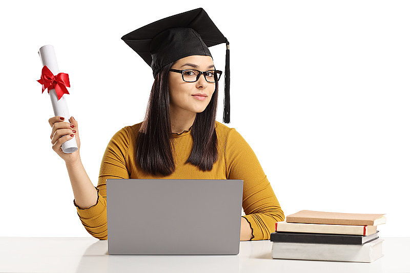 年轻女子戴着毕业帽，拿着毕业证书，坐着笔记本电脑和书
