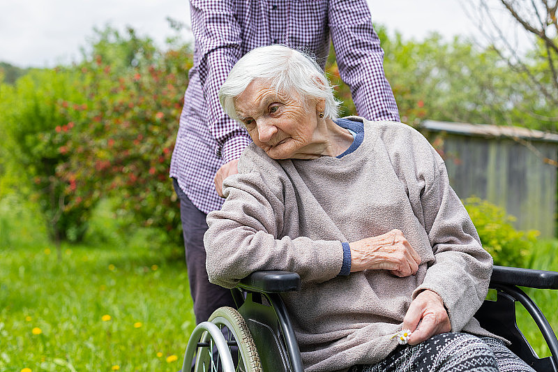 一位痴呆的老太太坐在轮椅上，还有人照顾她