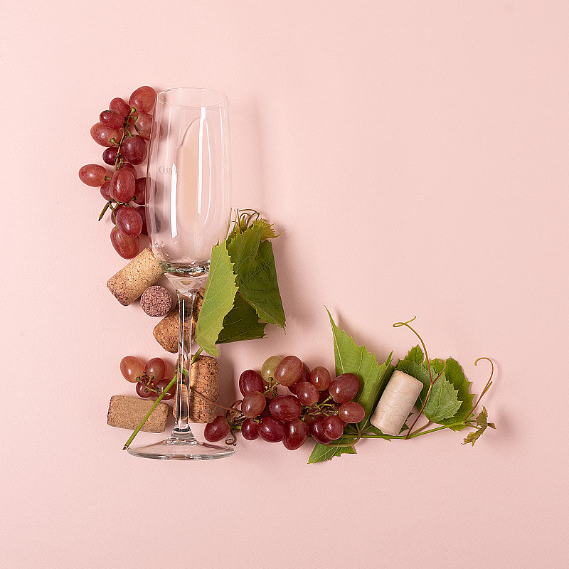 字母表。字母L是用葡萄酒杯、玫瑰和白葡萄酒、葡萄、树叶和软木塞在粉红色的背景上做成的。葡萄酒品尝的概念。平的。俯视图