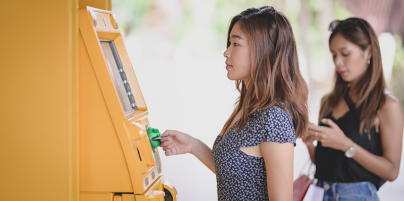 两个年轻的亚洲女性正在用ATM机从银行卡中取钱