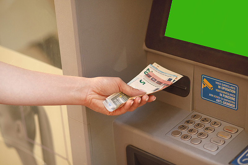 欧元纸币和自动取款机关闭。一个女人在外面从提款机里拿欧元。女性手拿欧元钞票