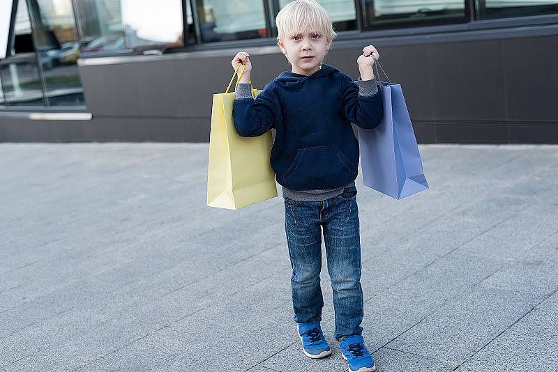 金发小男孩拿着购物袋。家庭购物