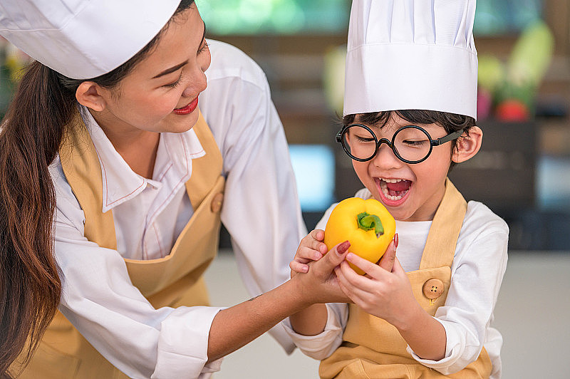 肖像可爱的小亚洲快乐男孩厨师感兴趣的烹饪与母亲有趣的家庭厨房。人们的生活方式和家庭。自制食物和配料概念。蔬菜沙拉制作