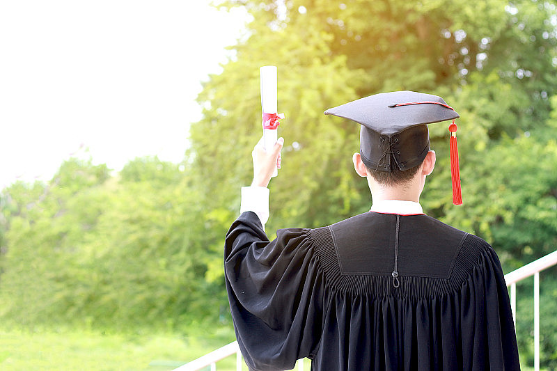 快乐毕业的学生戴着黑帽子，手拿证书完成大学学业，构想毕业日