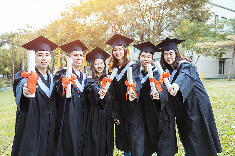 在大学校园里，快乐的学生们穿着毕业礼服，拿着毕业证书