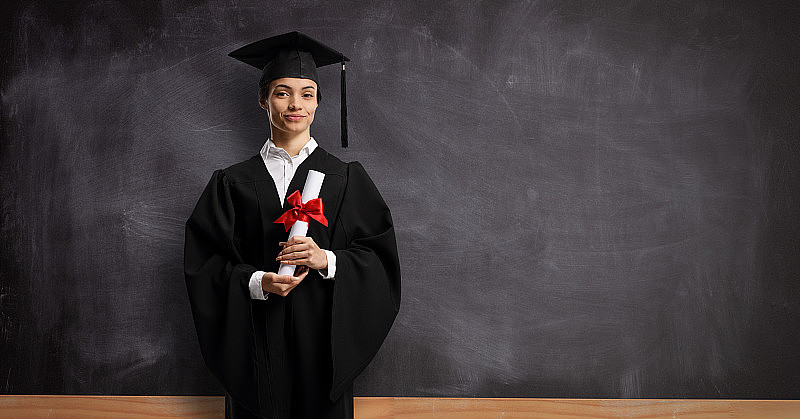 女学生穿着毕业礼服，拿着毕业证站在黑板前