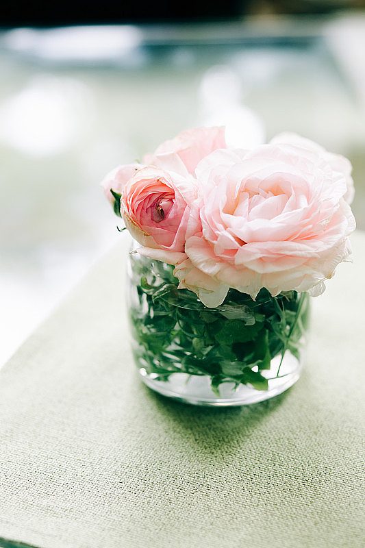 餐厅桌子上的一个小玻璃花瓶里装着精致的粉红色玫瑰