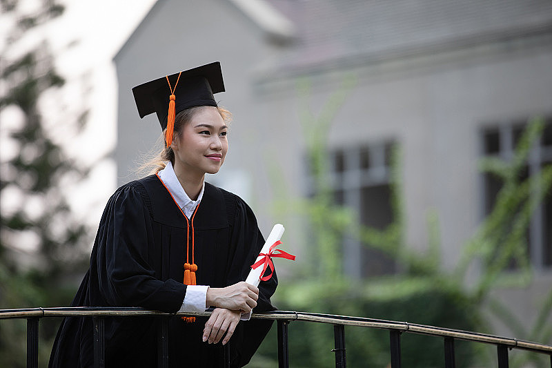 迷人的亚洲女学生毕业生戴着帽子和长袍，手拿证书庆祝，在毕业典礼上如此自豪的幸福，祝贺学生在毕业日，教育成功