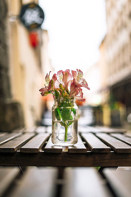 木桌上花瓶里的紫花。夏日咖啡馆桌上的玻璃花瓶里放着粉红色的花。