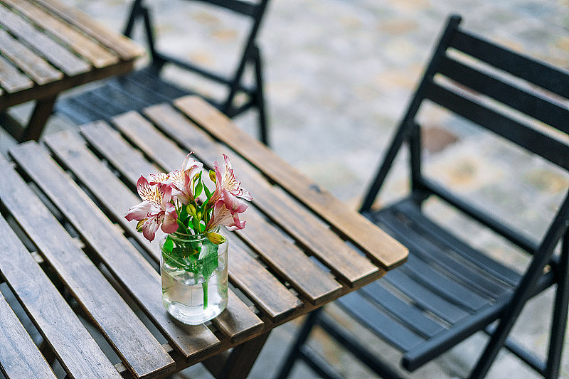 夏日咖啡馆的木桌上，花瓶里美丽的紫花蔷薇。玻璃花瓶里放着温柔的夏日花束。