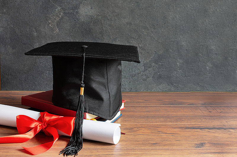 学位帽及毕业证书卷，并以红丝带系好。