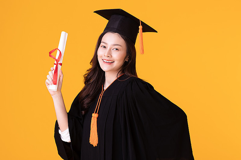 快乐毕业亚洲妇女在帽子和长袍持有证书或文凭黄色背景，夏季毕业概念