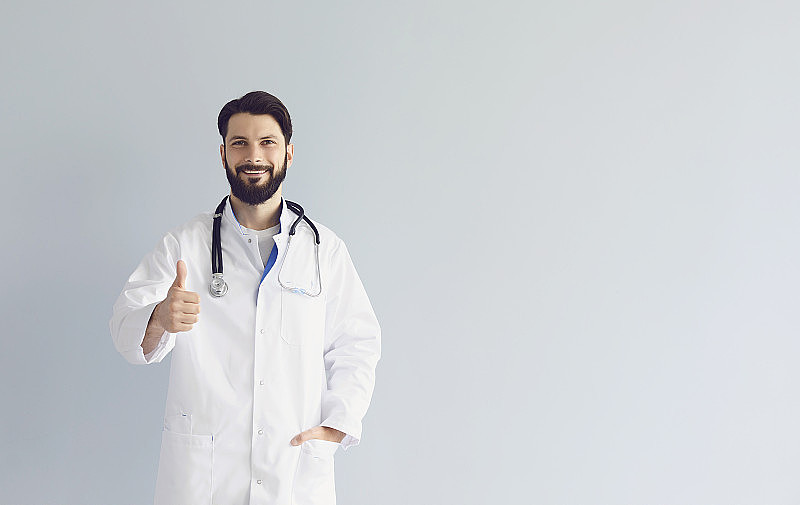 身穿制服的男医生在灰色背景上竖起大拇指，复制空间。治疗师批准医疗服务