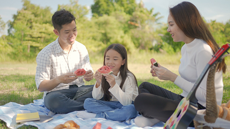 幸福的家庭亚洲和小女孩正在吃西瓜,并享受了我们自己一起在野餐布在