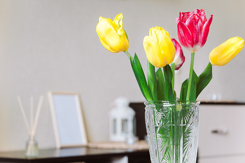 时尚家居装饰。一束黄色和粉红色的郁金香放在玻璃花瓶里。春天的室内装饰。放置你的文本。