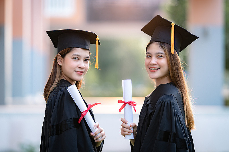 年轻快乐的亚洲女子大学毕业生在毕业礼服和学位证书持有学位证书庆祝教育成就在大学校园。教育库存图片