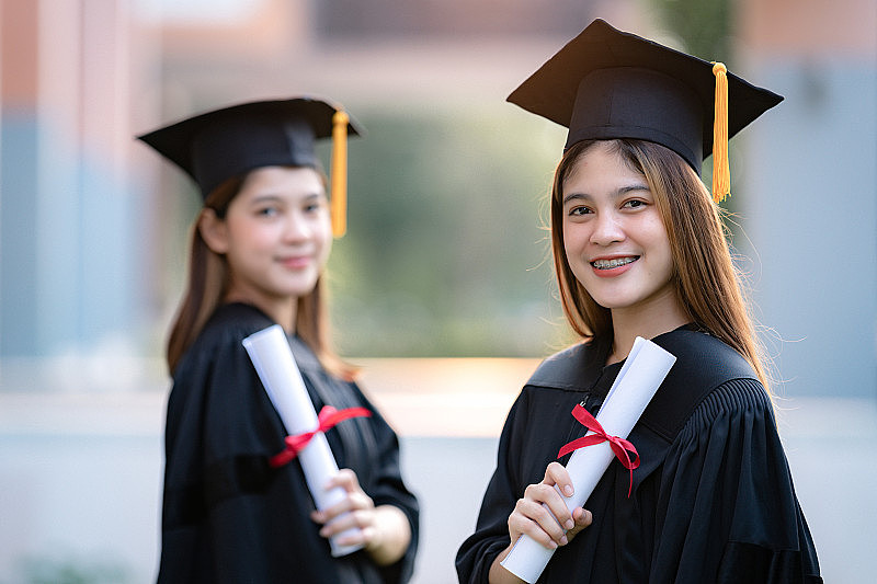 年轻快乐的亚洲女子大学毕业生在毕业礼服和学位证书持有学位证书庆祝教育成就在大学校园。教育库存图片