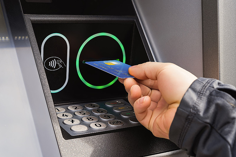 白种人的手插入信用卡ATM机。白天在街上从自动取款机里取钱。户外取现。使用银行自动取款机。