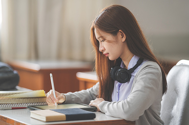 亚洲女大学生在大学教室里穿着学生制服在平板电脑上学习和写作的照片